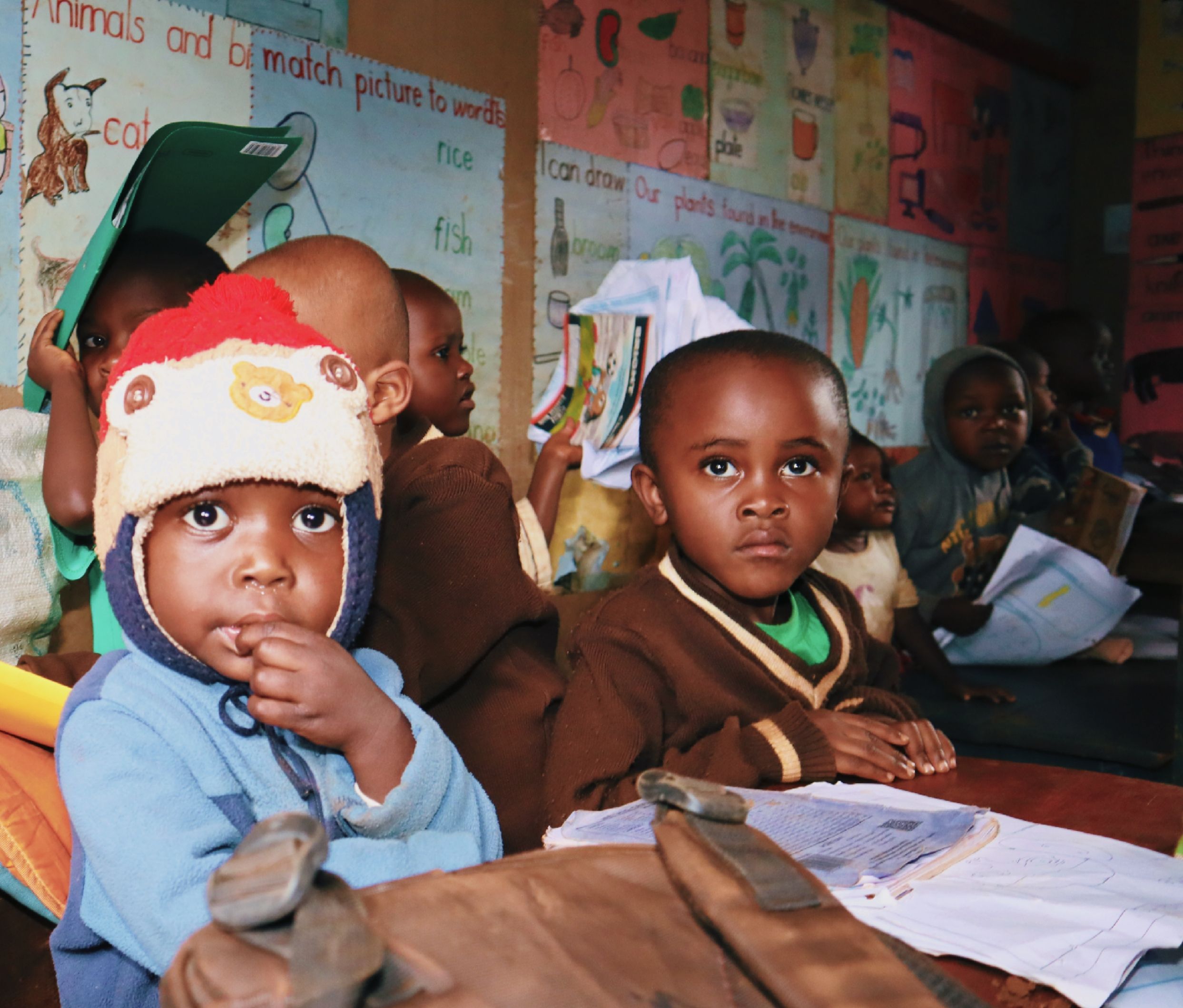 Young children sitting in a basic classroom with colourful handmade posters on the walls